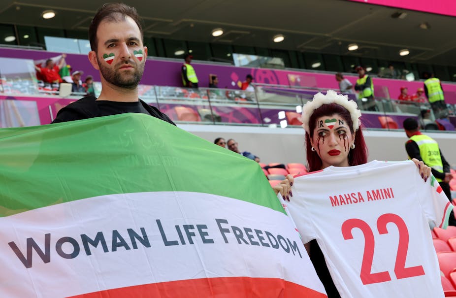 Supporters iraniens brandissant un maillot au nom de Mahsa Amini et un drapeau iranien barré de l'inscription « Woman Life Freedom »