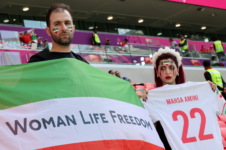 Supporters iraniens brandissant un maillot au nom de Mahsa Amini et un drapeau iranien barré de l'inscription « Woman Life Freedom »