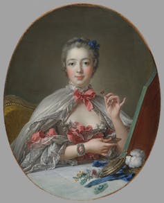 A painting of Jeanne-Antoinette Poisson, Marquise de Pompadour. She wears a cape fastened round her neck with a pink bow, over a pink dress and sits at her cosmetics table, applying blush to her face. Rather than look in the mirror, her gaze is on us.