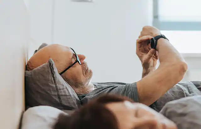 man lying in bed consults fitness tracker on his wrist
