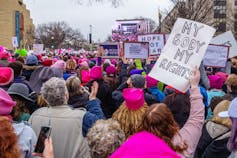 Protesters holding signs and wearing pink knitted beanie hats in the crowd at the Women's March in Washington DC.