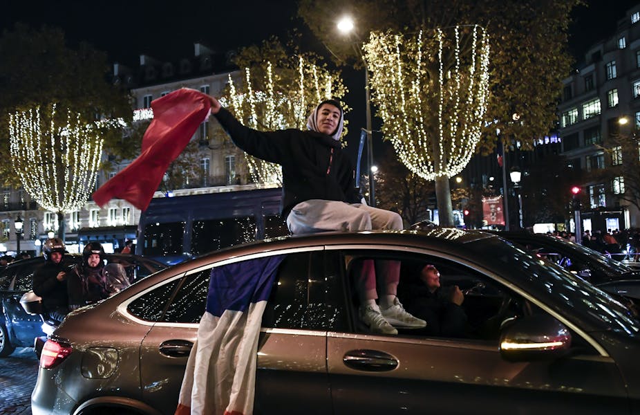 Un supporter agite un drapeau du Maroc assis sur le toit d'une voiture auquel est aussi accroché un drapeau de la France. Champs Elysées à Paris, le 6 décembre 2022.