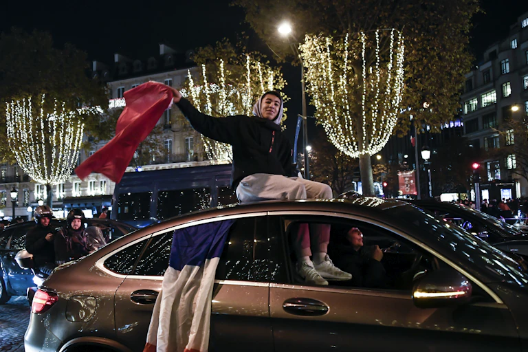 Un supporter agite un drapeau du Maroc assis sur le toit d'une voiture auquel est aussi accroché un drapeau de la France. Champs Elysées à Paris, le 6 décembre 2022.