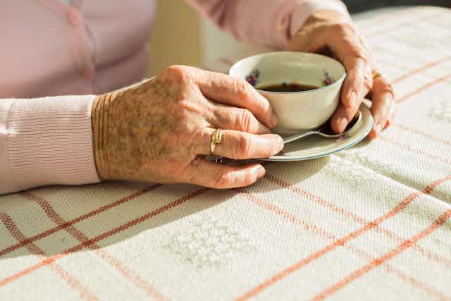 Hands of an elderly woman clasp a cup of coffee.