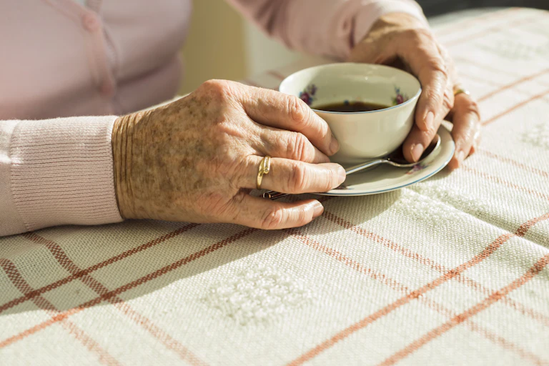 Hands of an elderly woman clasp a cup of coffee.