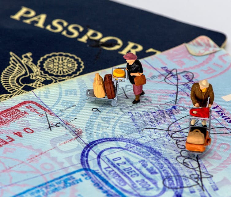 Tiny figures stand on the open pages of a stamped passport.