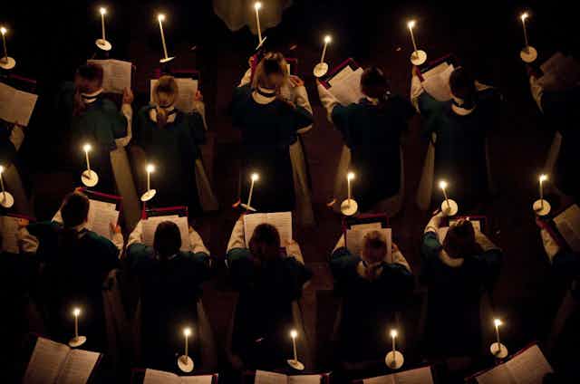Three rows of singers in robes holding music and lit candles.