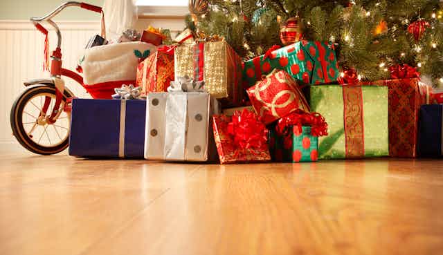 wrapped gifts of various colors and a bike sit on a hardwood floor under a Christmas tree