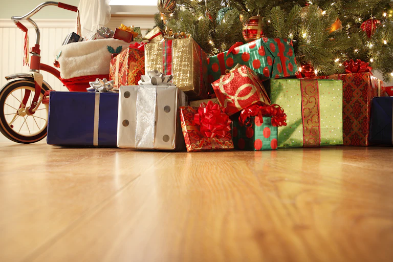 wrapped gifts of various colors and a bike sit on a hardwood floor under a Christmas tree
