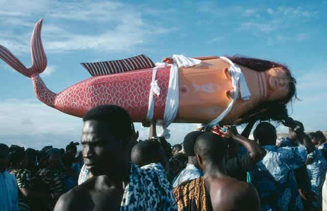 People hoist a coffin that resembles a mermaid.