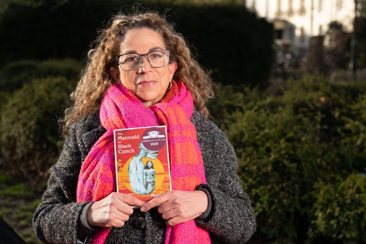 Woman wearing pink scarf holds book.