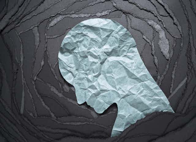Crumpled paper silhouette of a head against a background of torn black paper