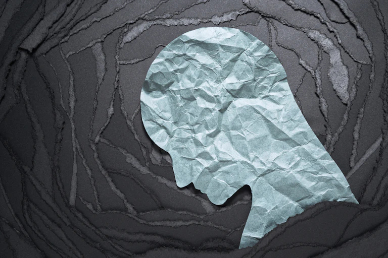 Crumpled paper silhouette of a head against a background of torn black paper