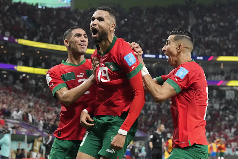 Three men in red and green soccer uniforms rejoicing on a packed stadium backdrop