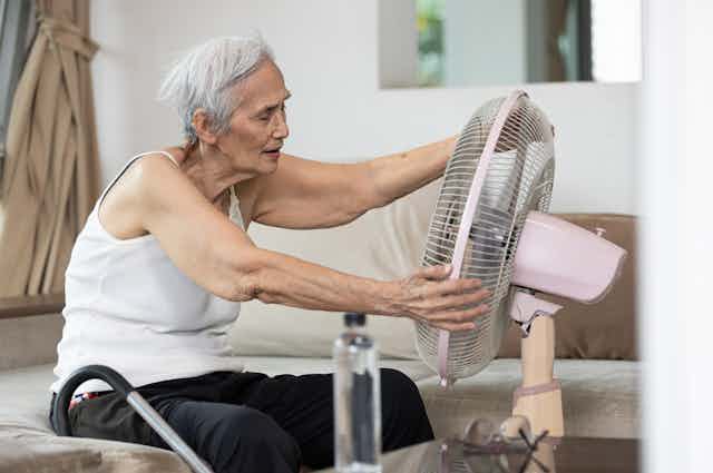 Elderly woman adjusting fan to keep cool