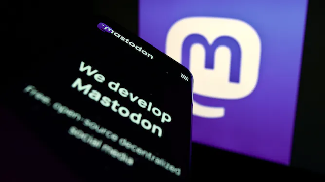 logo mastodon tampil di sebuah layar — huruf m biru dalam gelembung percakapan putih — ada layar ponsel yang menampilkan teks WE DEVELOP MASTODON