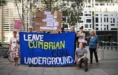 Protesters hold up a large blue sign that says
