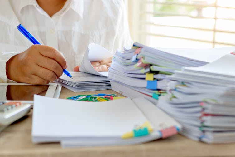 Hand with pen grading stacks of papers