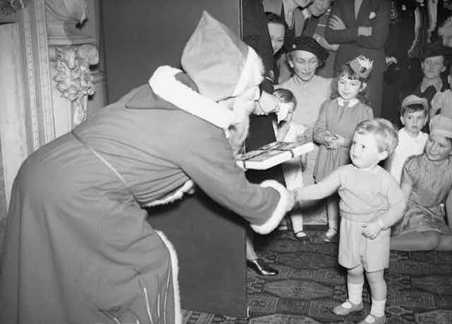 Father Christmas hands a present to a little boy at Christmas in wartime Britain.