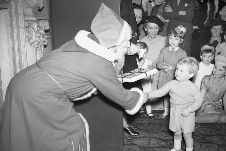 Father Christmas hands a present to a little boy at Christmas in wartime Britain.
