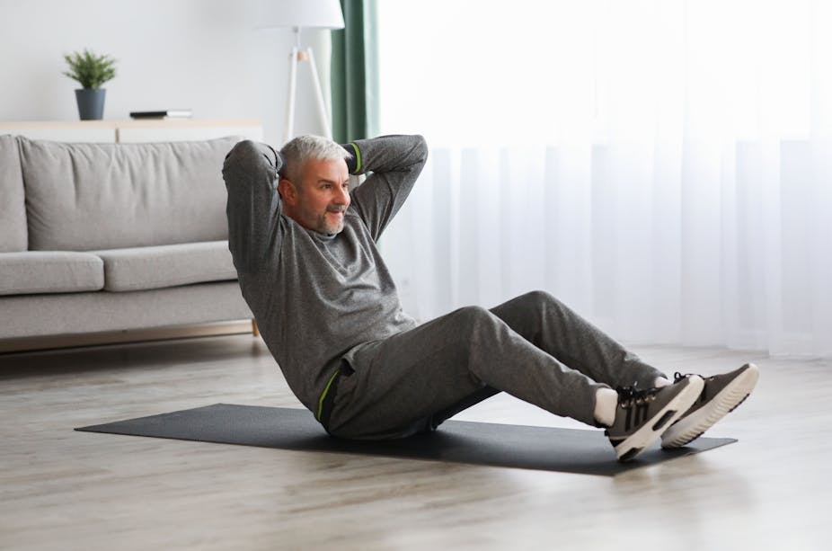 Older man does sit ups in his living room.