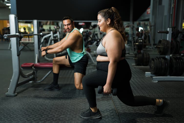 A woman performs a squat in the gym with her trainer.
