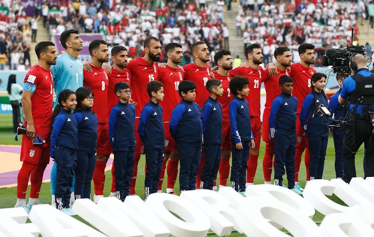 Iran's men's football team stands with children during their national anthem during a match at a stadium in Qatar, November 2022.