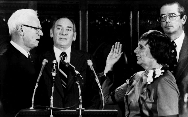 Three men and one woman, with her right hand raised, standing together during a ceremony.