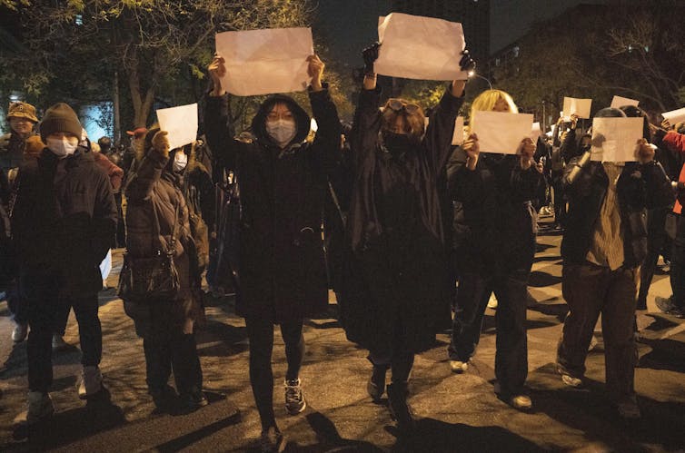 Protesters wearing masks march while holding up blank pieces of paper.