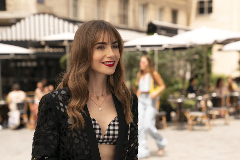 Emily stands in a Parisian courtyard wearing a blazer over a gingham bra.