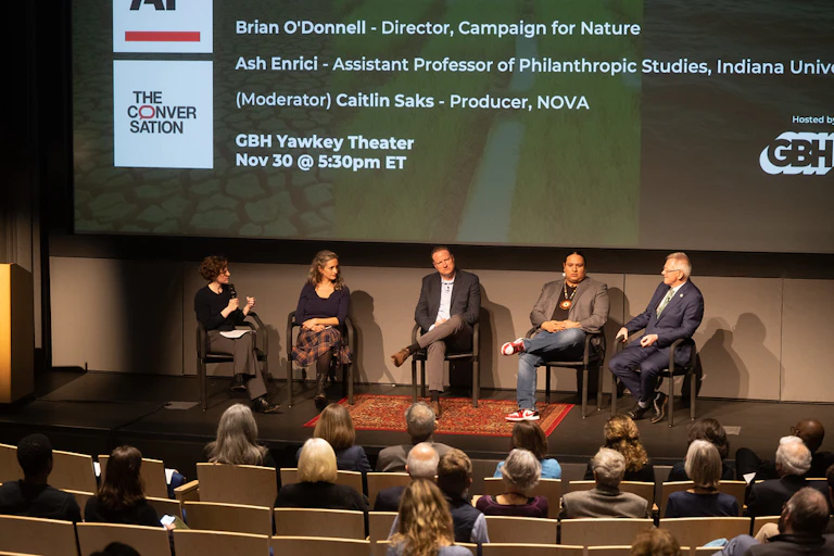 A panel of four people talking about climate in front of a big theater at GBH