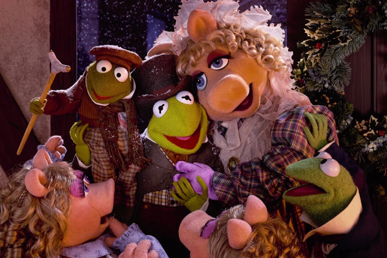Miss Piggy, Kermit and their children, two frogs and two piglets, embrace. They all wear Dickensian clothing.