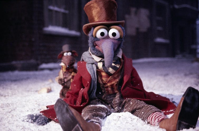 Gonzo sits in the snow wearing a Dickensian outfit, including a top hat. Rizzo the rat sits next to him in similar attire.