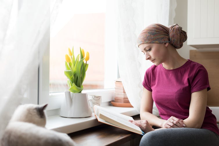 A woman wearing a head scarf is reading a book at home.