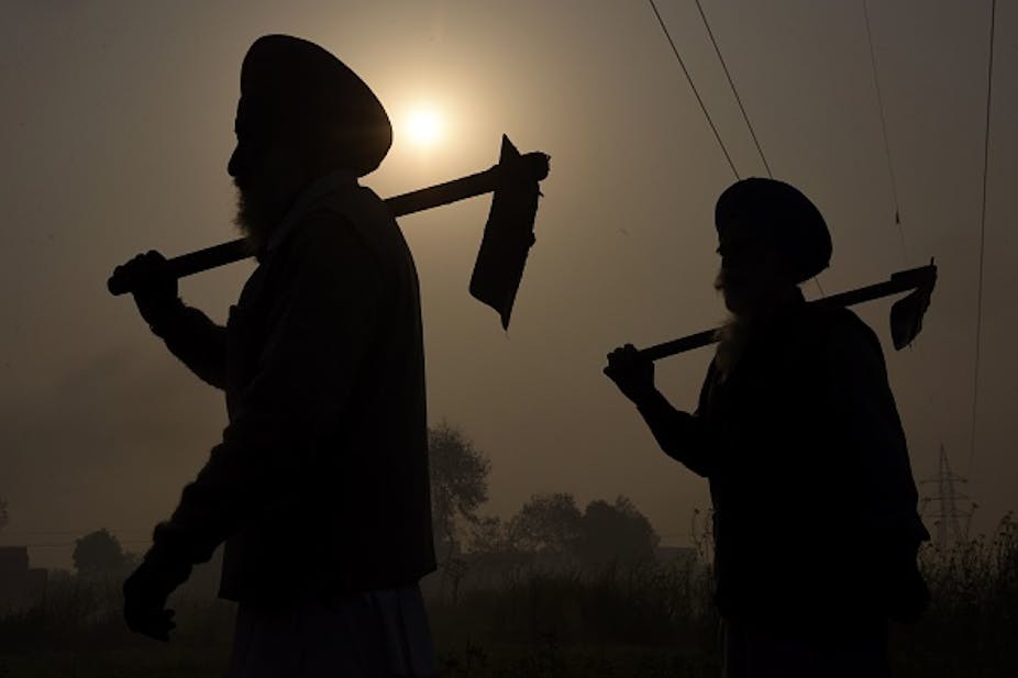 Two men with turbans on their heads carrying hoes are shown in silhouette