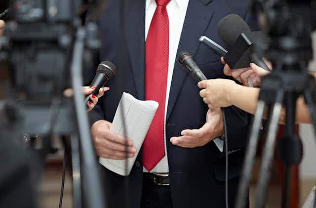 Reporters hold out microphones to a man in a suit and tie
