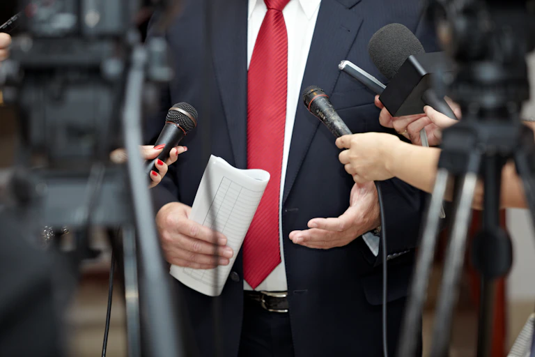 Reporters hold out microphones to a man in a suit and tie