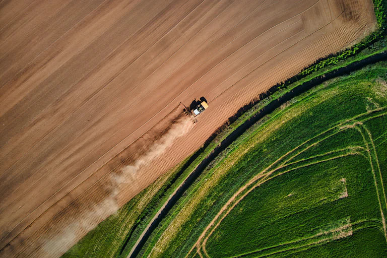 one green field, one dusty field with a farm vehicle driving through it