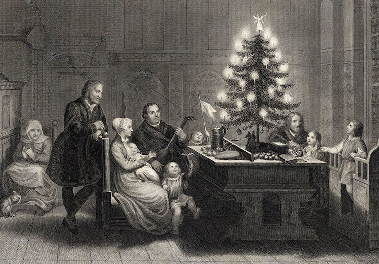 Engraving of adults and children gathered around a desk with a small Christmas tree adorned with candles