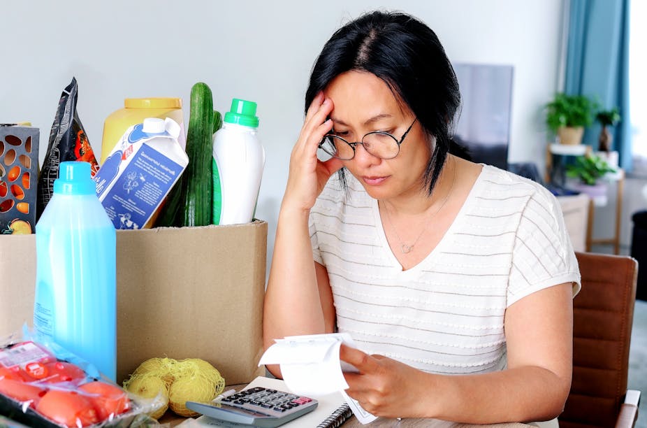 A woman holding receipts from supermarket with calculator, groceries in the background, finances, stress, worry.