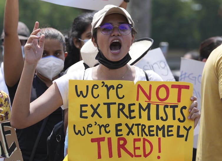 A young woman shouts while holding a sign that reads 'we're not extremists, we're extremely tired'