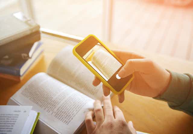 Close-up of a person's hands taking smartphone images of a textbook in a library