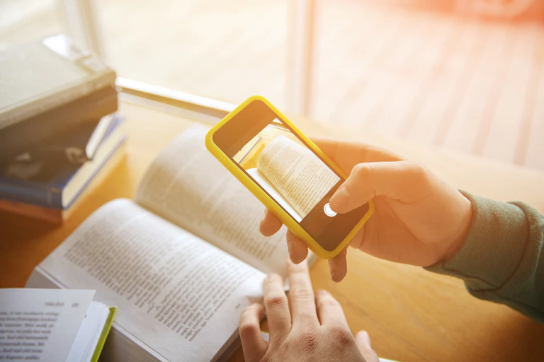 Close-up of a person's hands taking smartphone images of a textbook in a library