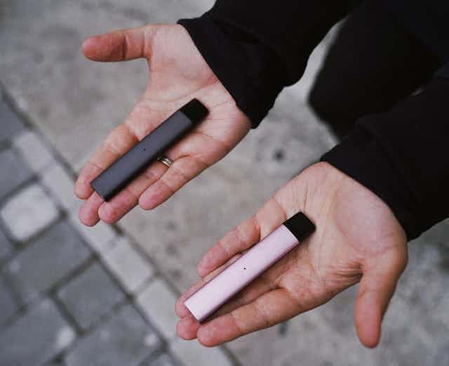Person holding two vapes, one in each hand, palm up