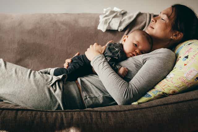 A woman lying on a sofa cradling a baby on her chest