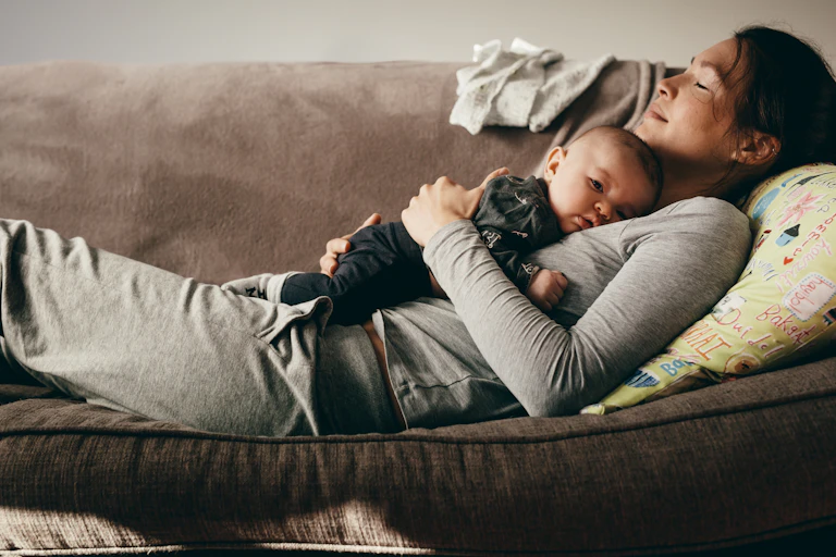 A woman lying on a sofa cradling a baby on her chest