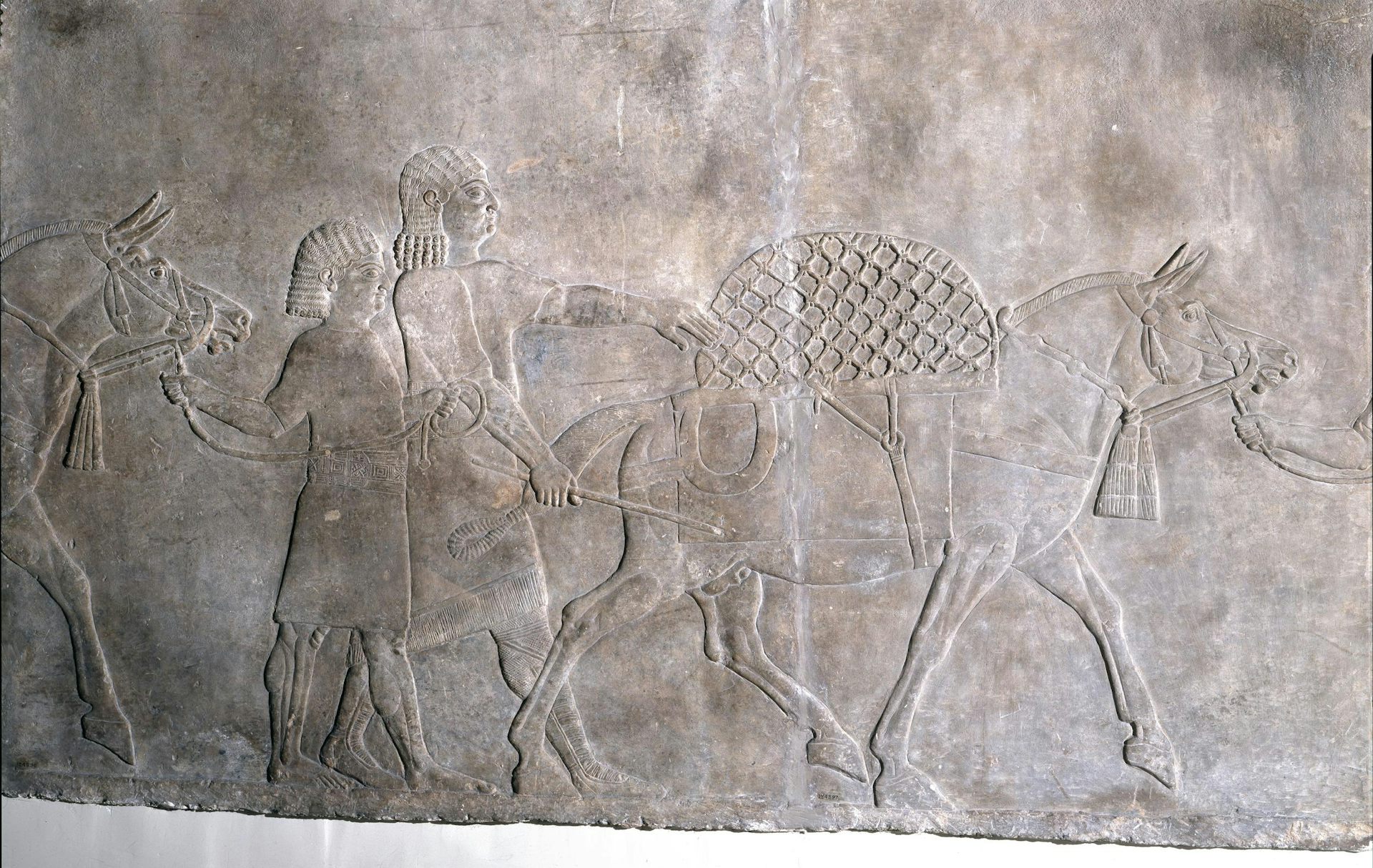 An ancient stone carving showing people with horses.