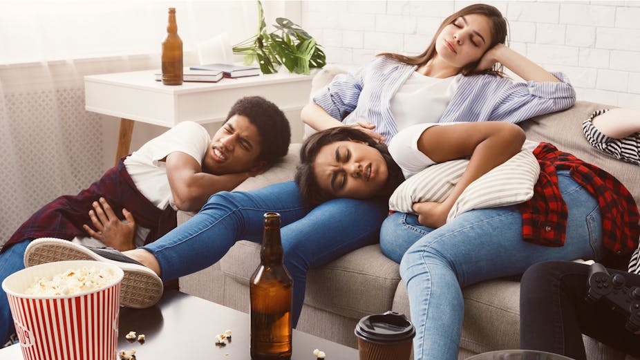 A young man and two young women lay on a couch in pain with hangovers.