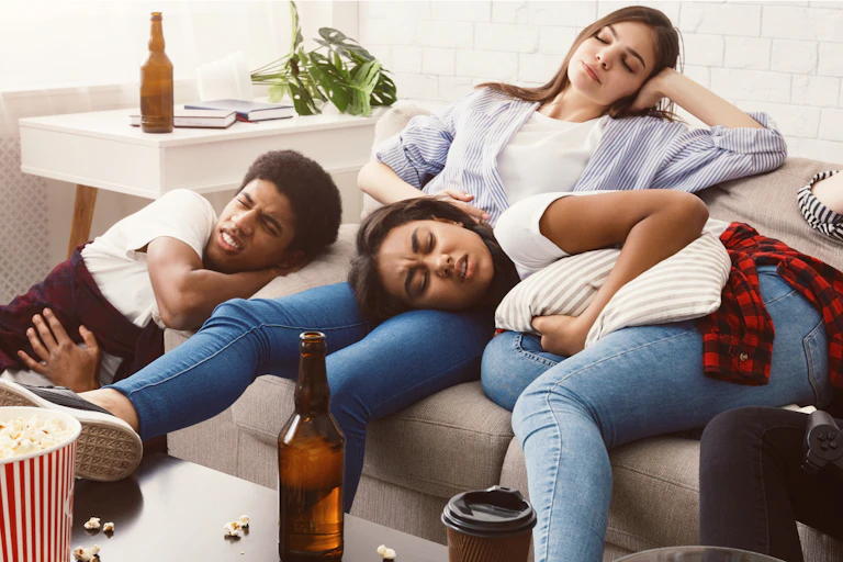 A young man and two young women lay on a couch in pain with hangovers.