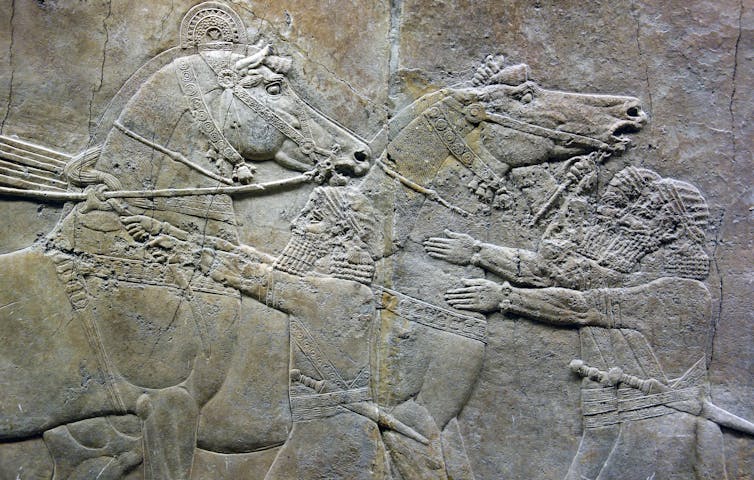 An ancient stone carving showing people with horses.